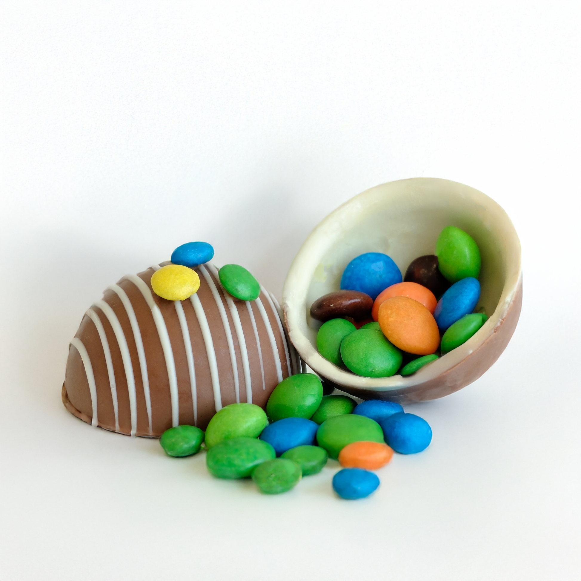 Chocolate egg with colorful candies spilling out on a white background