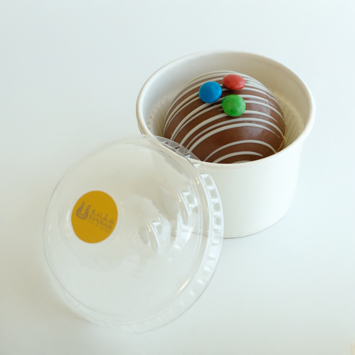 Chocolate donut with colorful sprinkles in a white container on a light background
