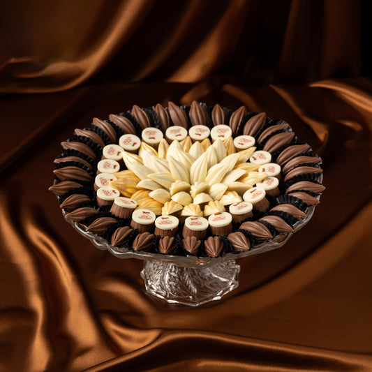 Decorative arrangement of Omani National Day chocolate tray with white chocolate and milk chocolate on a glass stand against a brown fabric background
