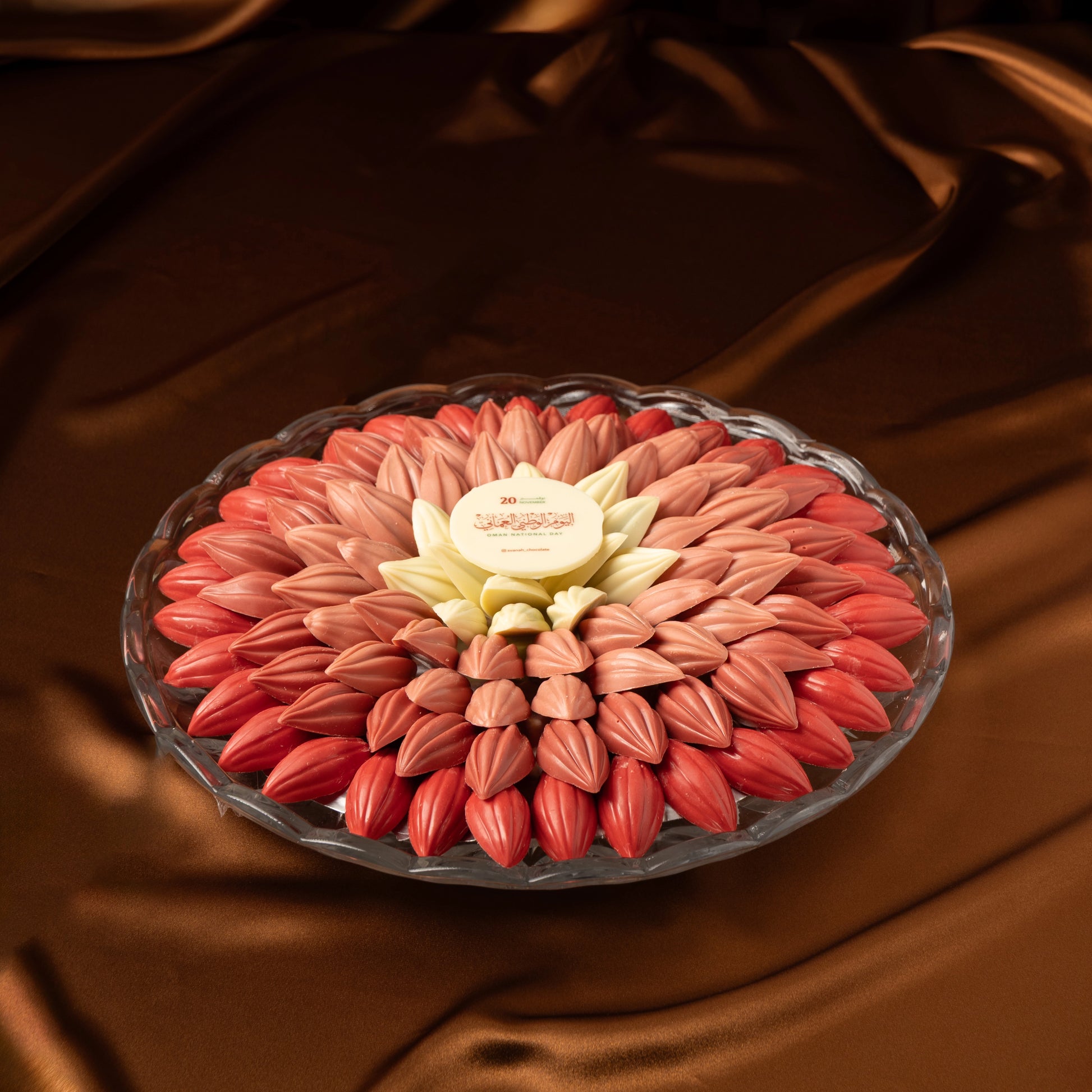 Omani National Day chocolate tray designed as red and pink flower-shaped chocolate on a brown fabric background
